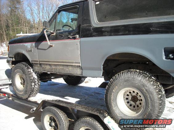 Gray and black Ford Bronco on a trailer, side view, showing lifted suspension and off-road tires