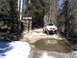 1987 Suzuki Samurai - A white Suzuki Samurai is parked on a dirt road in a wooded area, with a reflection visible in a puddle.