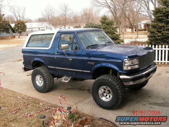 Blue lifted SUV with white top, parked in a driveway. Has large off-road tires and chrome wheels