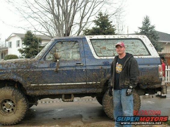 Mud-covered blue Ford Bronco with a white top, seen from the side