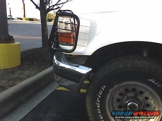 Front corner of a white SUV with a black headlight guard and chrome bumper