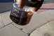 1990 Ford Bronco - A hand holds a glass jar filled with a dark, amber-colored liquid, possibly oil or fluid.