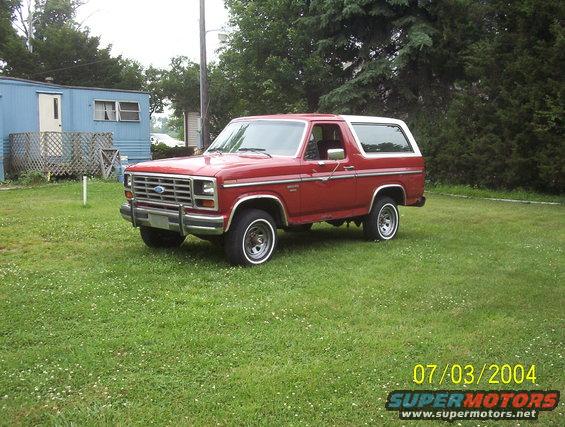 Red 1985 Ford Bronco with a white top parked on grass