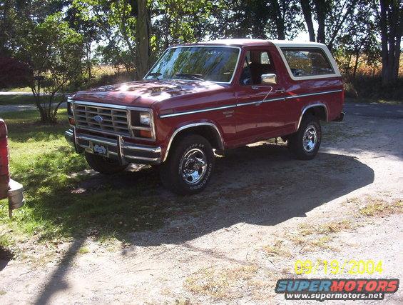 Red Ford Bronco parked outside on a sunny day. It has a white top and chrome wheels