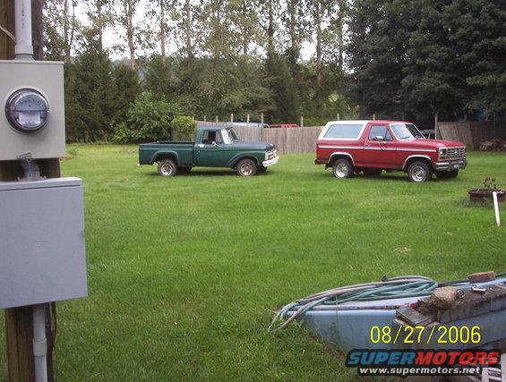 Red Ford Bronco parked on grass next to a green Ford F-100 truck