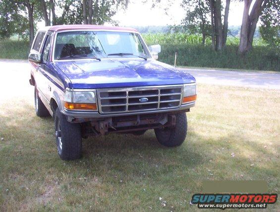 Blue Ford Bronco with a red top parked on grass, facing front