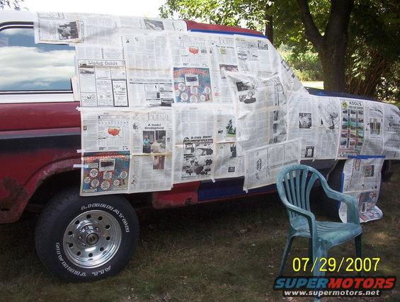 Red and blue truck body covered in newspaper for painting, with a green plastic chair in front