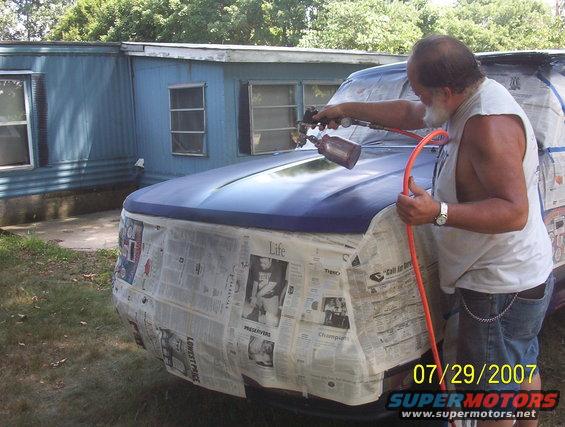 Man spray painting a blue SUV covered in newspaper