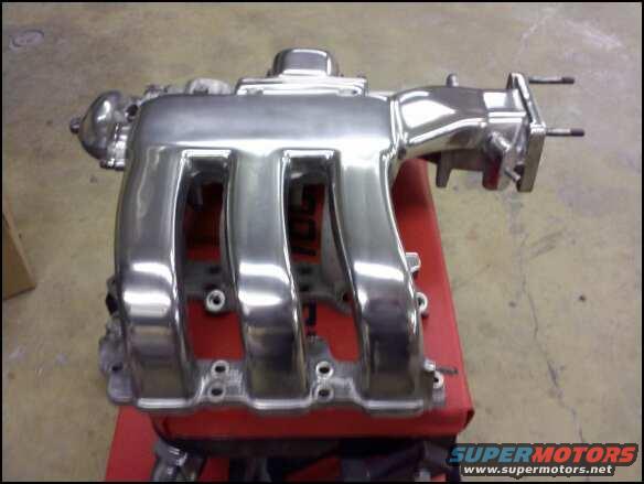 Polished aluminum intake manifold with four runners, mounted on a red stand