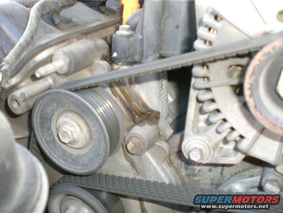 Close-up of engine belt tensioner and pulleys with a visible leak
