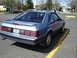 1986 Ford Mustang - The rear of a blue 1986 Ford Mustang coupe is shown parked in a lot with yellow lines.