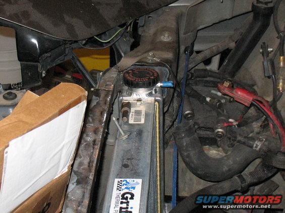 Car engine bay showing radiator, hoses, and wiring. Some parts are covered by a cardboard box
