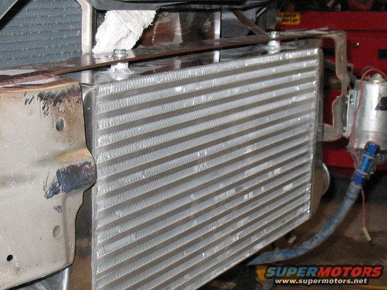 Aftermarket intercooler mounted in front of a radiator, with blue hose and wiring visible