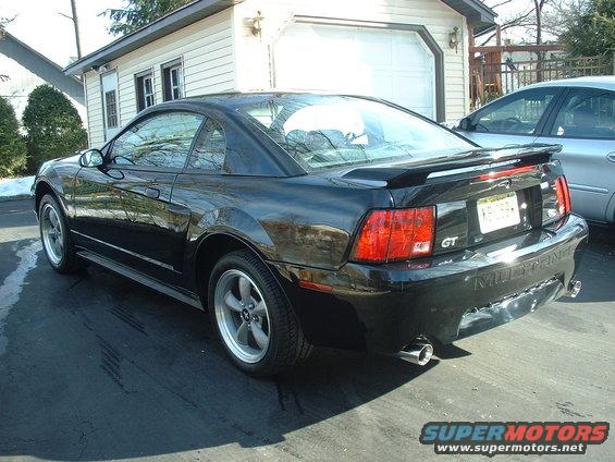 Black 2002 Ford Mustang GT coupe parked in driveway, rear view. Another car is visible to the right