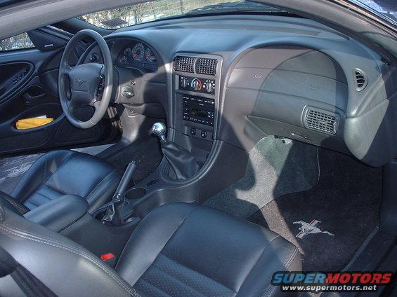 Interior shot of a 2002 Ford Mustang, showing black leather seats, dashboard, steering wheel, and gear shifter