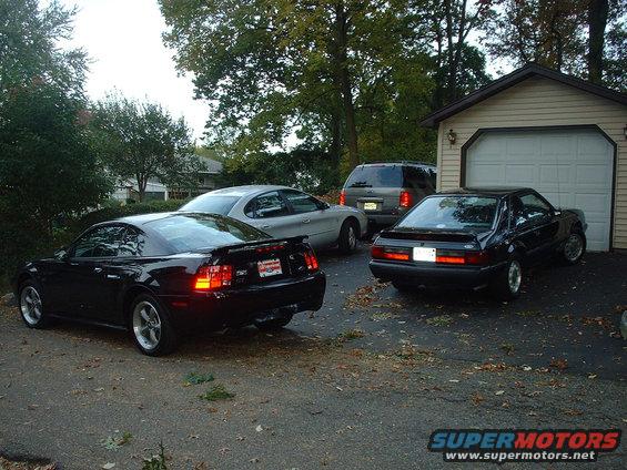 2002 Ford Mustang rear view, parked next to an older Mustang and an SUV