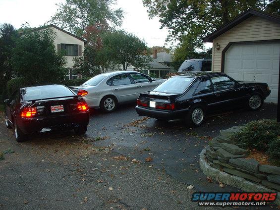 black coupe parked by garage, silver sedan and another car in driveway