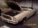 1977 Ford Mustang II - A white convertible is parked in a garage with its hood up, revealing the engine bay.