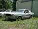 1976 Ford Mustang II - Two cars parked in front of a building, one is a 1976 Ford Mustang II coupe.