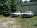 1977 Ford Mustang II - Three 1977 Ford Mustang IIs are parked outside a metal building, with trees in the background.