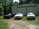 1977 Ford Mustang II - Three cars are parked in front of a large metal building. The cars are a black Mustang II, a white Mustang II, and a silver Mustang II.