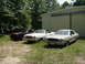 1977 Ford Mustang II - Three 1977 Ford Mustang IIs are visible in front of a large metal building with trees in the background.