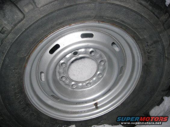 Close-up of a silver steel wheel with a knobby tire. Snow is visible around the wheel