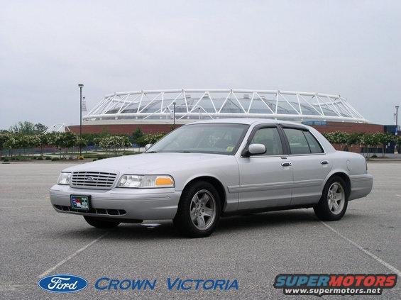Silver 2001 Ford Crown Victoria sedan parked in an asphalt lot with a stadium in the background