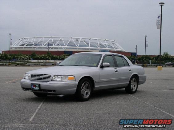 Silver 2001 Ford Crown Victoria parked in an empty lot with a stadium in the background
