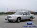 2001 Ford Crown Victoria - A silver 2001 Ford Crown Victoria is parked in an empty lot with a stadium in the background.