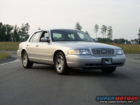 Silver 2001 Ford Crown Victoria sedan parked on asphalt road, trees and houses in background