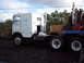 1981 Kenworth W900A - A white 1981 Kenworth W900A semi-truck is parked next to another truck, with trees and a cloudy sky in the background.