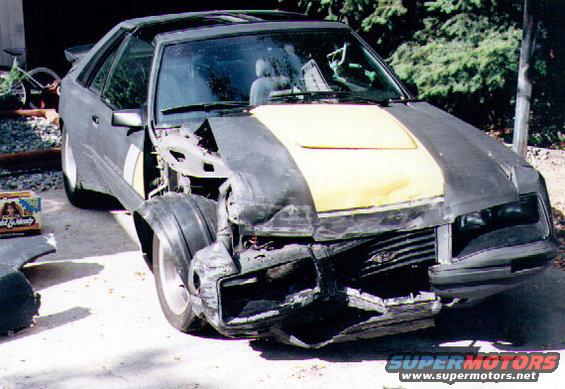 Front end of a damaged 1983 Ford Mustang SVO, showing extensive damage to the bumper and hood