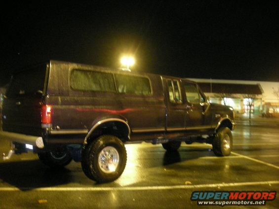 Dark purple Ford F-Series truck with a camper shell, lifted with large tires, parked at night