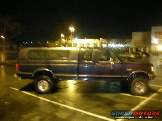 Side view of a dark blue crew cab pickup truck with a camper shell, lifted suspension
