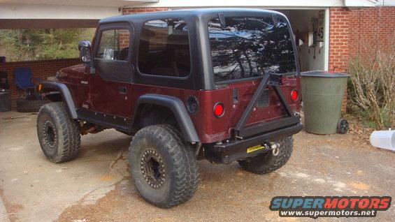 Maroon Jeep Wrangler with black hardtop and aftermarket rear bumper, parked in a driveway