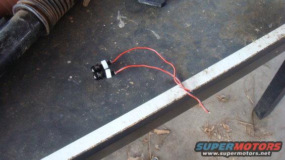 Two black LED tail lights with red wires on a workbench