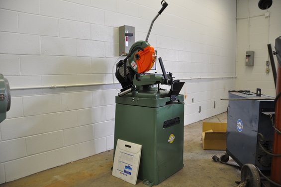 Green metal cutting saw with orange guard and a white document on the floor