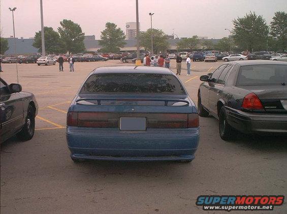 Blue sedan parked in a lot, rear view. It has a spoiler and tinted taillights