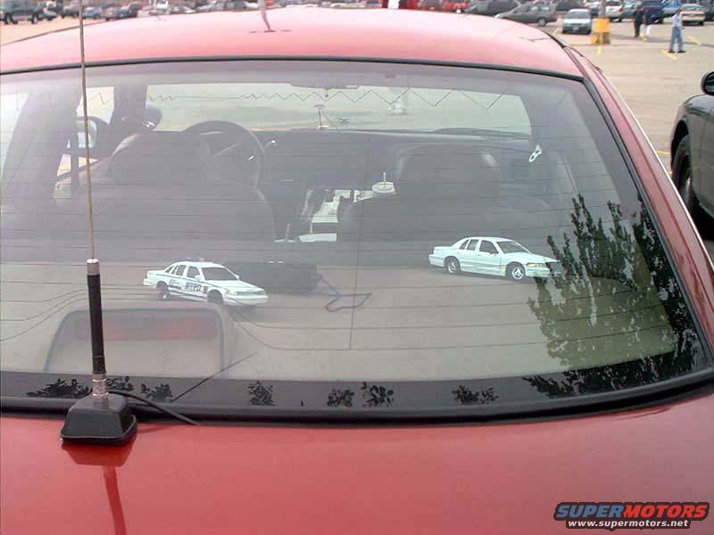 Two white police car models on a red car's rear window