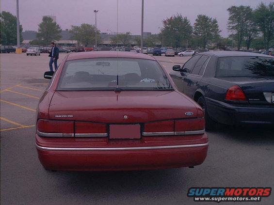 Rear view of a red 2000 Ford Crown Victoria parked next to a dark Ford Crown Victoria in a parking lot