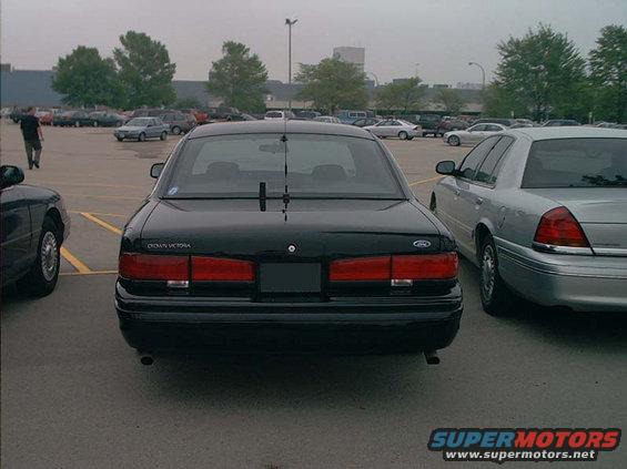 Rear view of a black Ford Crown Victoria parked next to a silver Crown Victoria. Text on the trunk reads 'CROWN VICTORIA'