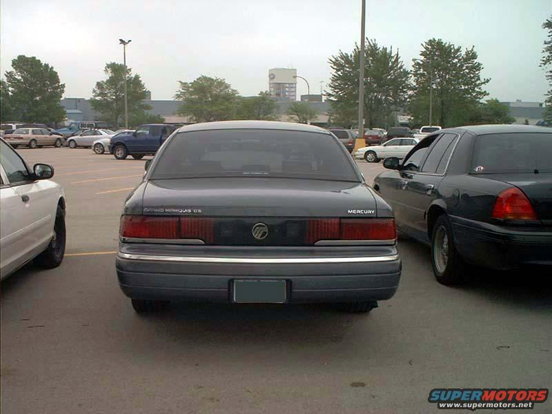 Rear view of a dark gray Mercury Grand Marquis parked between two other cars. The car has a chrome bumper and taillights. Text on the trunk reads 'MERCURY'