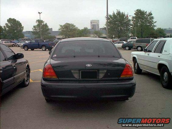 Rear view of a black Ford Crown Victoria parked in a lot. Another car is to its left, and a white car is to its right