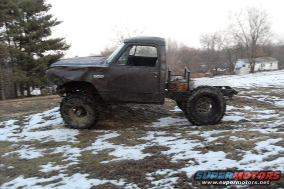 Lifted pickup truck with a dented front end and no bed, sitting in a snowy field