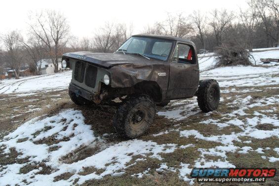Brown Dodge pickup truck with damaged front end and large off-road tires, parked on a snowy hill