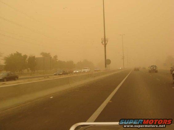 Highway traffic obscured by a sandstorm, with multiple cars visible on the road and a watermark at the bottom