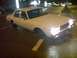 1998 Ford Crown Victoria - A white sedan is parked on a wet street at night with its headlights illuminated.