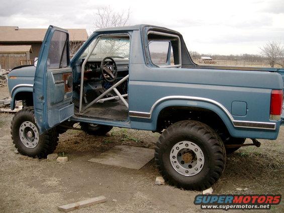 Blue SUV with roll cage, lifted suspension, and large tires. Doors are open, showing the interior