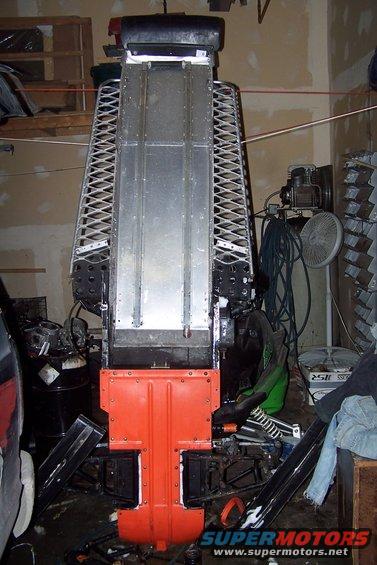 Snowmobile chassis with orange front guard and metal track bed, in a garage